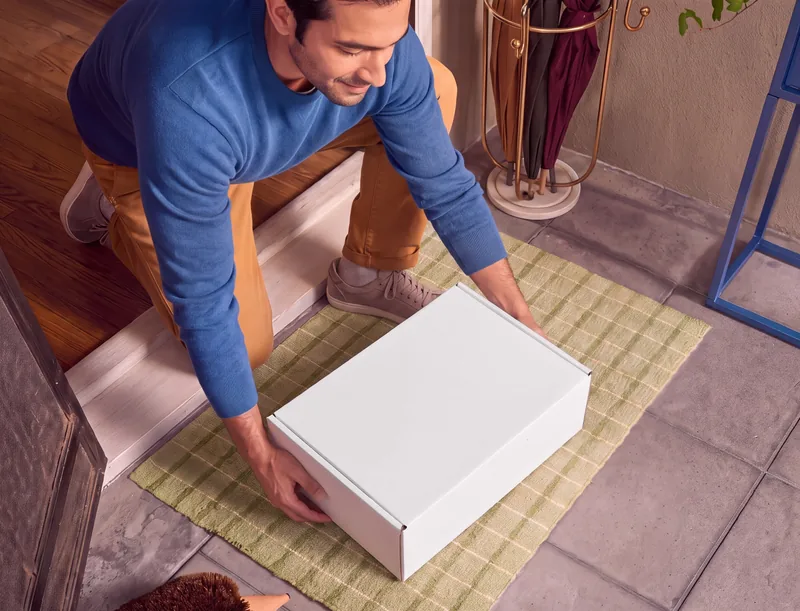 A man lifting a white HeMed delivery box from his doormat